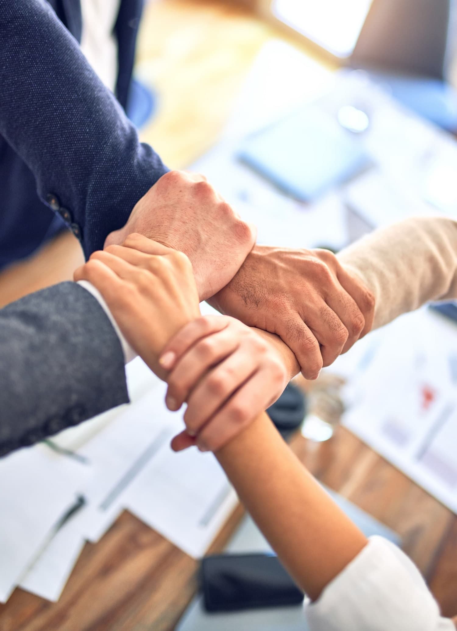 Group of 4 business workers standing holding hands together in the office