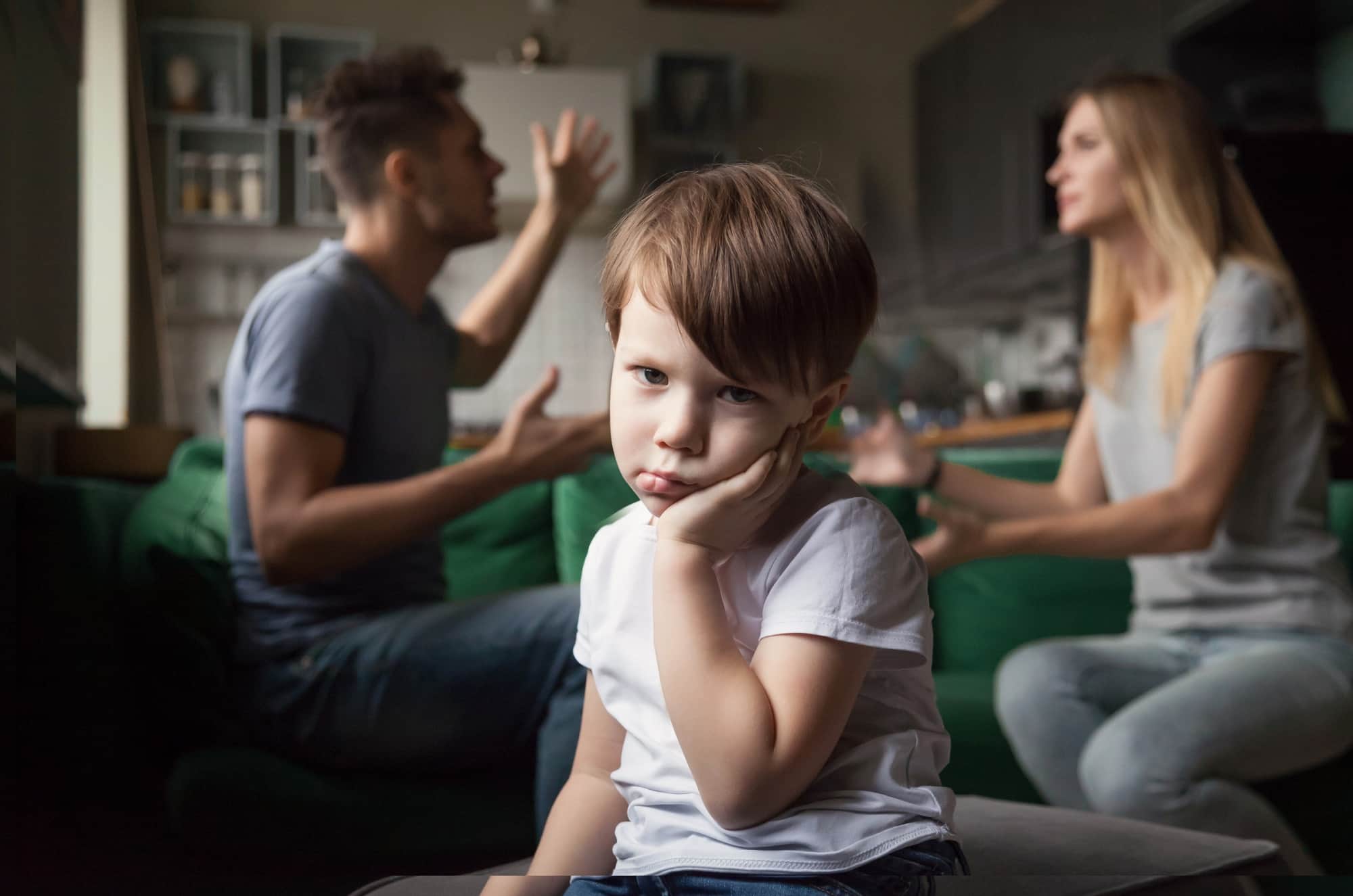 Young boy with a sad facial expression in the foreground, with his parents arguing behind him Young boy with a sad facial expression in the foreground, with his parents arguing behind him
