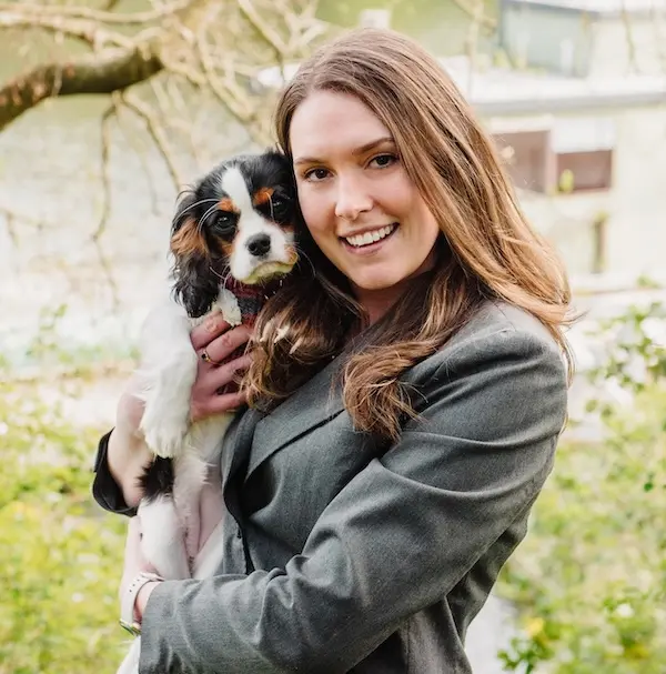 Diana Illy from Pathway Legal in a grey blazer holding a small black, white, and tan dog called Lady Maya outdoors