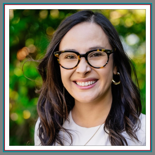 Professional outdoor headshot of Viviana Vargas, Legal Assistant at Pathway Legal, smiling brightly wearing tortoiseshell glasses, gold hoop earrings, and a white top against a soft green background.