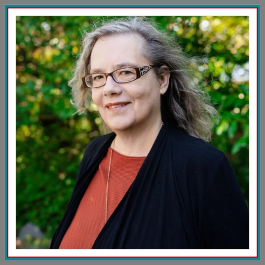 Professional outdoor headshot of Ana Simeon, family lawyer at Pathway Legal, smiling warmly with silver hair, rectangular glasses, a rust top, and black cardigan against a green garden background.