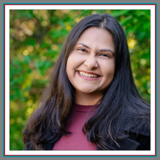 Professional outdoor headshot of Anu Singh, family lawyer at Pathway Legal, smiling with long dark hair, wearing a mauve ribbed top and black jacket against a bright green background.