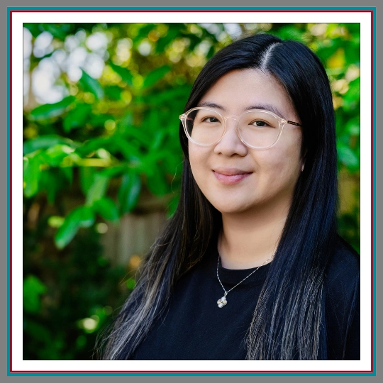 Professional outdoor headshot of Celine Ilano, Chief Herding Officer at Pathway Legal, smiling softly with long dark hair, clear frame glasses, and a delicate necklace against a green leafy background.