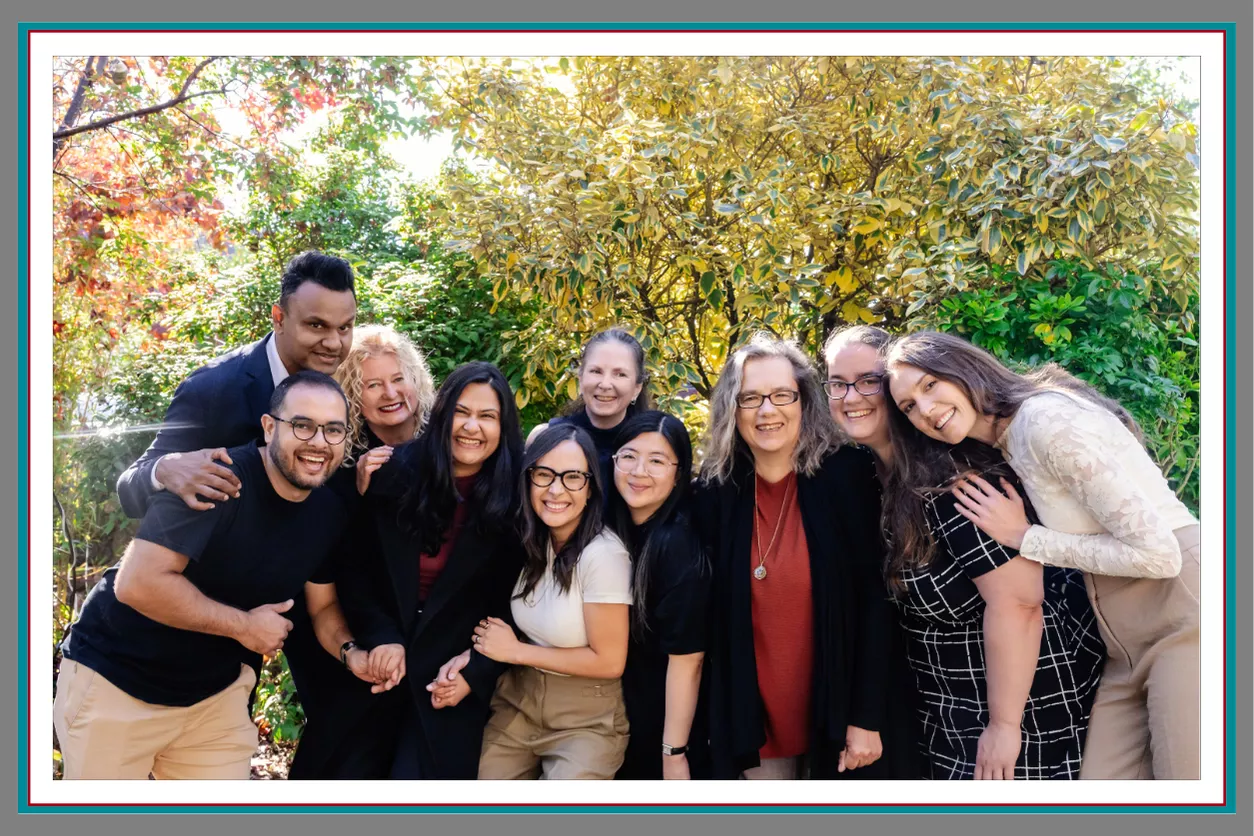 A joyful close-up group photo of the Pathway Legal team huddled together laughing and smiling outdoors among vibrant autumn foliage in gold, red, and green, capturing the warmth and genuine connection of the Pathway Legal pack in Fall 2026.